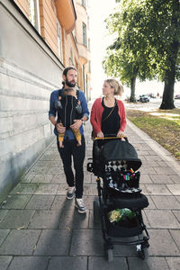 Mid adult parents with baby boy and carriage walking on sidewalk