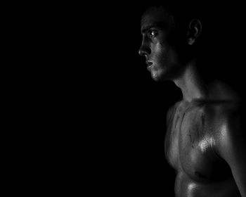 Close-up of shirtless young man against black background