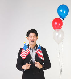 Portrait of smiling young man holding balloons against white background