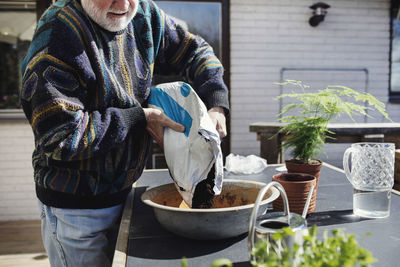 Midsection of senior man pouring mud in container at table on sunny day