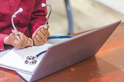 Cropped image of doctor holding stethoscope while using laptop in hospital