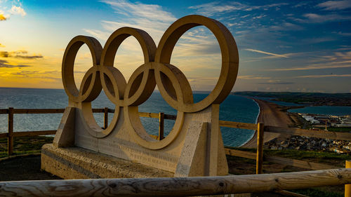Metallic structure on beach against sky during sunset