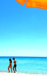 Friends on beach against clear blue sky