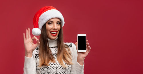 Portrait of smiling young woman using phone against red background