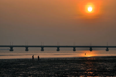 Silhouette bridge over sea against sky during sunset