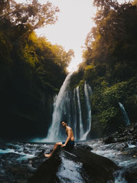 Young woman standing by waterfall in forest