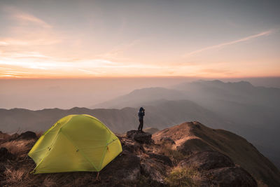 Tourist photographing while camping on mountains against sky during sunset