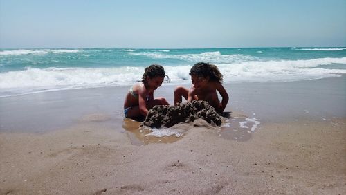 Friends playing with sand at beach against clear sky