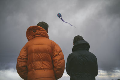 Low angle view of father and son flying kite against stormy clouds