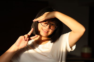 Close-up portrait of young woman shielding eyes while gesturing at home