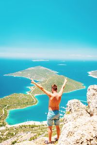 Full length of shirtless man standing by sea against blue sky