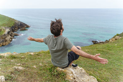 Rear view of boy standing on rock by sea against sky