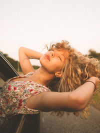 Young woman leaning from car window against clear sky