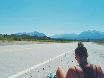 Rear view of woman sitting on road against clear blue sky