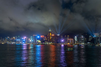 Illuminated buildings by river against sky at night