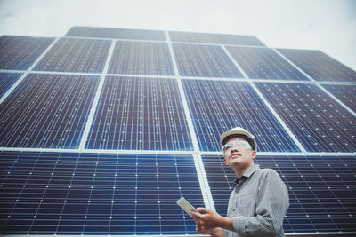 Low angle view of man holding digital tablet while standing against building