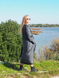 Young woman standing by plants against sky