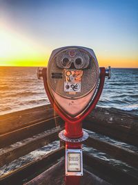 Close-up of coin-operated binoculars by sea against sky during sunset