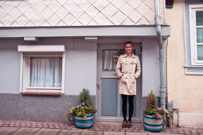 Portrait of young woman standing by house