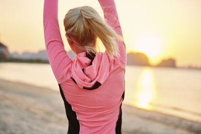 Rear view of woman standing by sea against sky during sunset