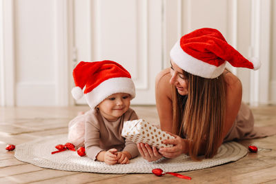 Happy family,  mom and baby little daughter in red santa hats celebrate christmas together at home