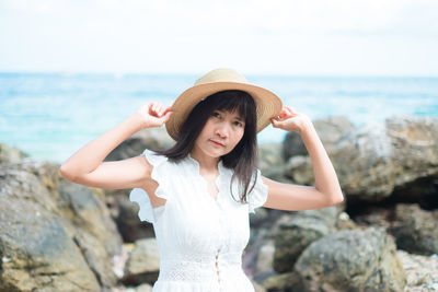 Portrait of beautiful young woman on rock at sea shore