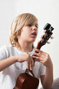 Young boy tuning ukulele at home. blond haired boy sitting on couch playing acoustic guitar.