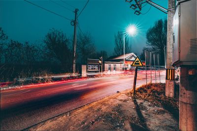 Illuminated railroad tracks by road against sky
