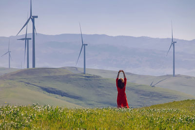 Woman enjoying clean air on the green meadow with wind turbines on the background. 