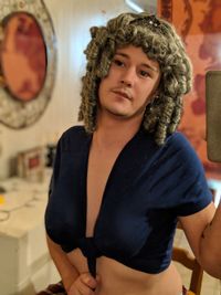 Portrait of man wearing wig and crop top while sitting at home