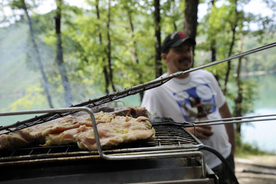 Close-up of meat cooking on barbecue grill with man standing in background