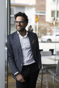 Smiling male real estate agent leaning on glass door in office