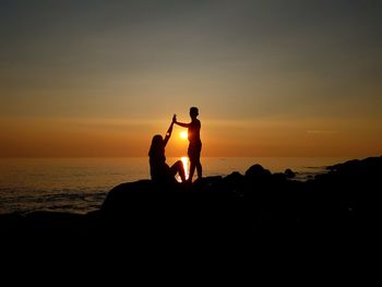 Silhouette men on beach against sky during sunset