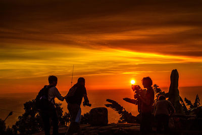 Silhouette people at beach against sky during sunset