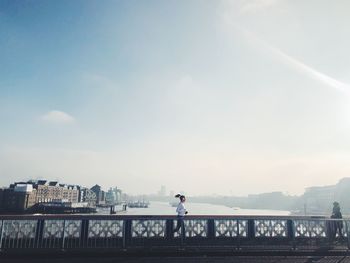 Runner on bridge over river in city against sky