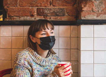 Portrait of young woman standing against brick wall