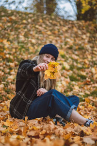 Smiling and happy brunette sitting in a pile of colourful leaves in a city park