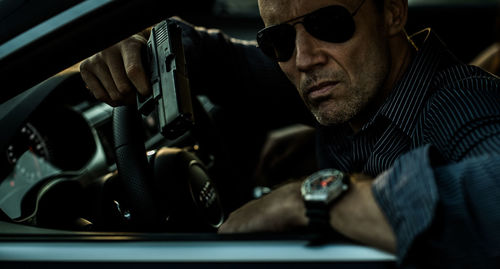 Close-up of man holding gun while sitting in car