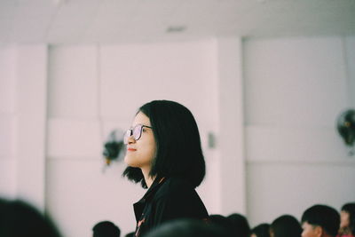 Side view of woman wearing eyeglasses while standing against wall