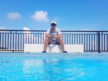 Young woman sitting on swimming pool against blue sky