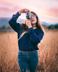 Portrait of young woman photographing on field