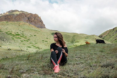 Portrait of young woman sitting on field against sky