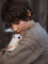 Cute little boy in gray knitted sweater holds a small white rabbit in his arms.