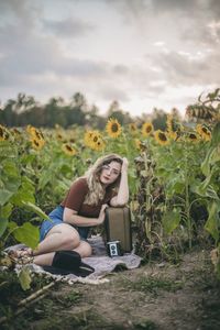 Portrait of young woman sitting on field amidst flowers during sunset