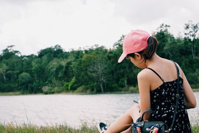 Side view of young woman sitting against trees