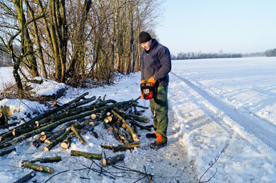 Lumberjack holding saw while standing by logs on snowy field