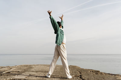 Young man dancing on pier in front of sky and sea