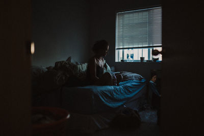 Woman sitting on bed at home in the dark in combination and worrying deep thought