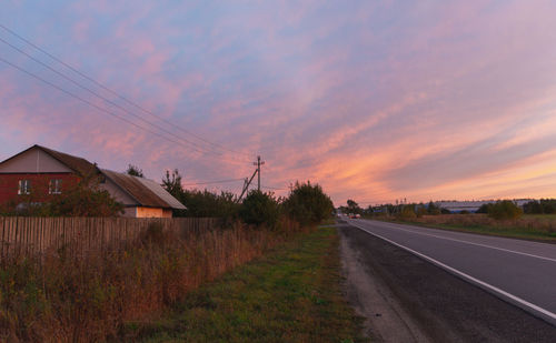 Road amidst field against sky during sunset