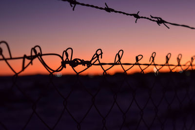 Silhouette of barbed wire fence against sky during sunset